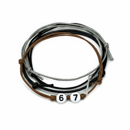 Black 67 meme bracelets set made of layered black, gray and brown cord bracelets with white number beads reading ‘67.’ This adjustable waterproof bracelet pack is a piece of 67 jewelry inspired by the viral 6-7 hand gesture, the 6-7 kid Maverick trend and TikTok’s Gen Alpha meme aesthetic, ideal for stacking, sharing and everyday school outfits.
