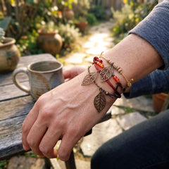 Falling Leaves bracelets worn on a wrist beside a mug in a garden setting