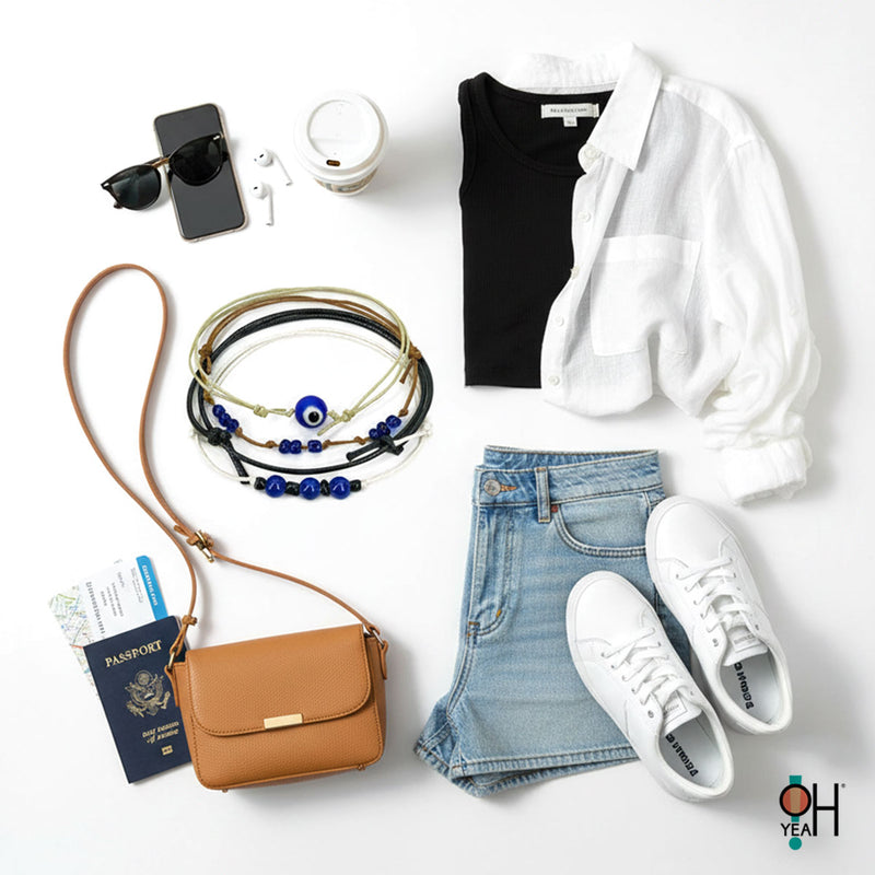 Flat lay of a chic travel outfit with black tank and white button-up shirt, light denim shorts, white sneakers, tan crossbody bag with passport and boarding pass, smartphone, sunglasses, earbuds and coffee cup surrounding a blue evil eye cord bracelet stack from O Yeah Gifts; evil eye bracelet, protective charm jewelry, lifestyle jewelry image, ai jewelry image, ai bracelet photo, product photography jewelry, trend jewelry photography.