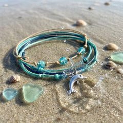 Green Dolphin Bracelet Style Pack on wet sand with sea glass and shells, the dolphin charm catching a splash