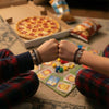 Two friends in plaid pajamas doing a fist bump over a board game night with pizza and chips, both wearing matching black and brown 67 string bracelets from O Yeah Gifts, cozy lifestyle jewelry image of a 6-7 meme bracelet that makes kids ask what is 6 7 and what does 67 mean, perfect 67 trend bracelet and school-safe friendship bracelet gift for teens who want an IYKYK six seven meme accessory.