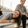Teen girl having fun on metal bleachers at sunset, smiling at the camera while wearing a brown 67 string bracelet stack from O Yeah Gifts, 6-7 meme bracelet and IYKYK accessory for teens, six seven meme jewelry inspired by the 6-7 TikTok trend and gen alpha 6-7 slang, school safe bracelet and school friendly accessory that fits the friendship bracelet trend, stackable teen bracelets and matching bracelets teens can trade, viral 67 trend bracelet and six seven funny gift you can buy 6-7 bracelet online.