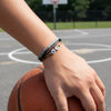 Close-up of a hand resting on a basketball, stacked with gray, black and brown 67 bracelets with white 6 and 7 beads from O Yeah Gifts, bracelet macro photo and product photography jewelry shot of a subtle 6-7 meme bracelet, ideal for shoppers searching what is 6 7, what does 67 mean and buy 6-7 bracelet online and trend jewelry photography for hoopers who love the 6-7 TikTok. 