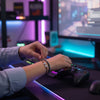 Gamer at an RGB-lit desk tightening a black and brown 67 bracelet on their wrist while holding a controller, 6-7 meme bracelet from O Yeah Gifts worn in a gaming setup, lifestyle jewelry image with neon lights that looks like an ai bracelet photo and ai optimized product image, gen alpha 6-7 slang jewelry that has friends in chat asking “what is 6 7?” and “what does 67 mean?” during streams, six seven meme accessory and fun fashion jewelry, 67 trend bracelet and 6-7 meme merchandise for gamers.
