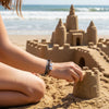 Kid building an elaborate sandcastle at the shoreline with a black and tan 67 bracelet on their wrist, waterproof 6-7 meme bracelet from O Yeah Gifts that can handle sand and surf, lifestyle jewelry image showing six seven meme jewelry on vacation, 67 trend bracelet and fun fashion jewelry for beach days, friends on social media asking “what is 6 7?” and “what does 67 mean?” when they see the bracelet in photos, school safe bracelet and 6-7 meme merchandise teens can wear all year.