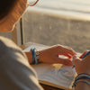 Teen drawing or journaling by a sunny window while wearing stacked ocean blue 67 bracelets from O Yeah Gifts, lifestyle jewelry image of a school-safe 6-7 meme bracelet that fits everyday outfits, beach bracelets, perfect 67 trend bracelet and fun friendship bracelet for gen alpha kids whose friends keep asking what is 6 7 and what does 67 mean when they spot the beads.