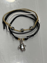 Black penguin bracelet stack on white: 4 adjustable string bracelets in black, white, beige with a silver-tone penguin charm.