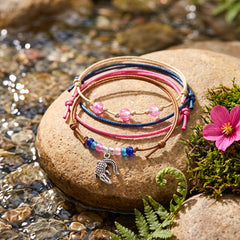 Pink Alligator Bracelet Style Pack stacked on a sunlit river stone beside a pink flower, moss and a fern