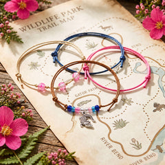 Four bracelets from the pink Alligator Bracelet Style Pack laid out on a wildlife park trail map with pink flowers