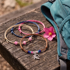 Pink Alligator Bracelet Style Pack on a weathered wooden bench next to a teal backpack and a pink flower