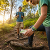 Teens hiking on a forest path, one adjusting a camera while both wear layered green 67 bracelets from O Yeah Gifts, lifestyle jewelry image and trend jewelry photography that looks like an ai jewelry image from a catalog; these 6-7 meme bracelets are worn by gen alpha kids who laugh when people ask “what is 6 7?” and “what does 67 mean?” because the six seven meme accessory is their IYKYK signal, fun fashion jewelry, school safe bracelet, 67 trend bracelet and 6-7 friendship bracelet gift.