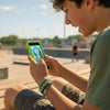 Teen boy at a skatepark checking his phone while wearing a green 67 string bracelet from O Yeah Gifts, lifestyle jewelry image and fun fashion jewelry shot that feels like an ai jewelry image and ai bracelet photo, trend jewelry photography for the viral 6-7 meme bracelet and six seven slang accessory; kids around him keep asking “what is 6 7?” and “what does 67 mean?” as the IYKYK joke from the 6-7 TikTok trend, school safe bracelet and school friendly accessory, 67 trend bracelet and 6-7 meme merchandise 