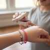 Close up of a tween girl’s wrist wearing a pink 67 bracelet pack from O Yeah Gifts with pink, light pink and brown adjustable string cords and white beads reading 6 and 7 while a friend holds out a small gift box, 6-7 meme bracelet and six seven meme accessory, six seven funny gift for the 6-7 TikTok trend, what does 6-7 mean slang jewelry answer, viral 6-7 trend accessory and gen alpha funny slang bracelet, school safe bracelet and school friendly accessory for the friendship bracelet trend, tradeable gift