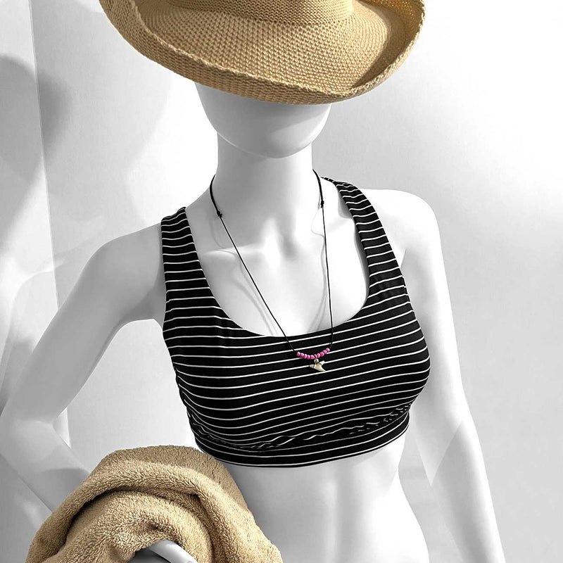 Woman wearing adjustable pink shark tooth necklace long over striped swimsuit with beach towel and straw hat – boho beach jewelry style for summer