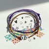 Flat lay of a purple 67 bracelet circle on paper covered with stars, doodles and washi tape, creative desk scene showing a 6-7 meme bracelet from O Yeah Gifts as an artsy six seven funny gift, pixel vibe bracelet and neon vibe bracelet style cords, 6-7 meme accessory for teens who love journaling and stickers, gen alpha meme jewelry for the 67 trend, school safe bracelet and viral gen alpha accessory, 6-7 meme merchandise and 6-7 jewelry that fits the friendship bracelet trend, 67 vibe trending.