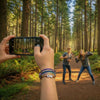Teen taking a photo of friends on a forest trail while wearing a stacked purple 67 bracelet from O Yeah Gifts, lifestyle jewelry image and ai bracelet photo style that shows a fun 6-7 meme bracelet in the wild; perfect for gen alpha kids whose friends keep asking what is 6 7 and what does 67 mean, six seven meme jewelry and 67 trend bracelet for hikers and campers, school safe friendship bracelet gift for teens who love inside jokes and outdoor adventures.