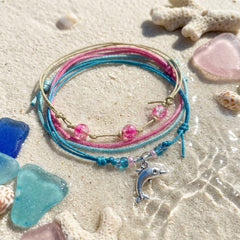 Dolphin Bracelet Style Pack Pink on wet sand with sea glass and coral, the silver dolphin charm catching the light.