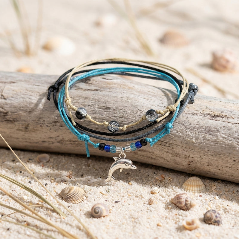 Black Dolphin Bracelet Style Pack draped over driftwood on pale sand with seashells and dune grass
