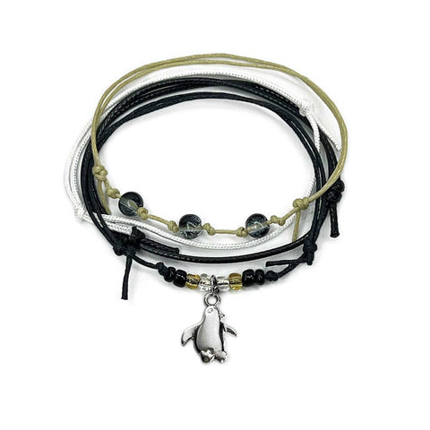 Black penguin bracelet stack on white: 4 adjustable string bracelets in black, white, beige with a silver-tone penguin charm.