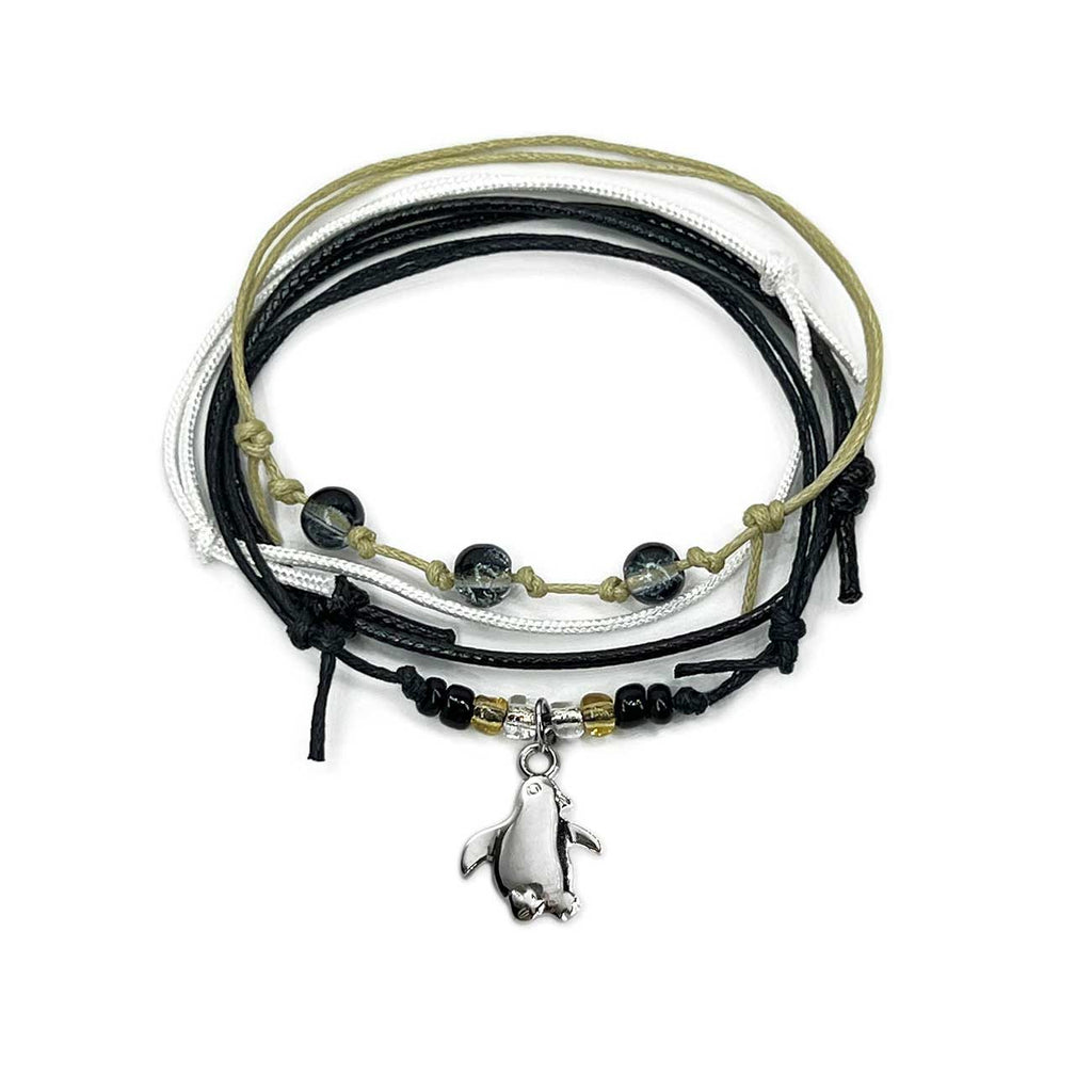 Black penguin bracelet stack on white: 4 adjustable string bracelets in black, white, beige with a silver-tone penguin charm.