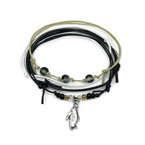 Penguin Bracelet Style Pack: 4 black, white and beige bracelets with a silver-tone penguin charm, flat lay on white