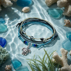 Black Sea Turtle Bracelet Style Pack in shallow water on pale blue sand with sea glass, coral and shells