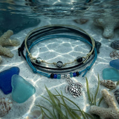 Black Sea Turtle Bracelet Style Pack underwater on the sand with sea glass, coral and sea grass in rippling light