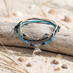 Black Dolphin Bracelet Style Pack draped over driftwood on pale sand with seashells and dune grass