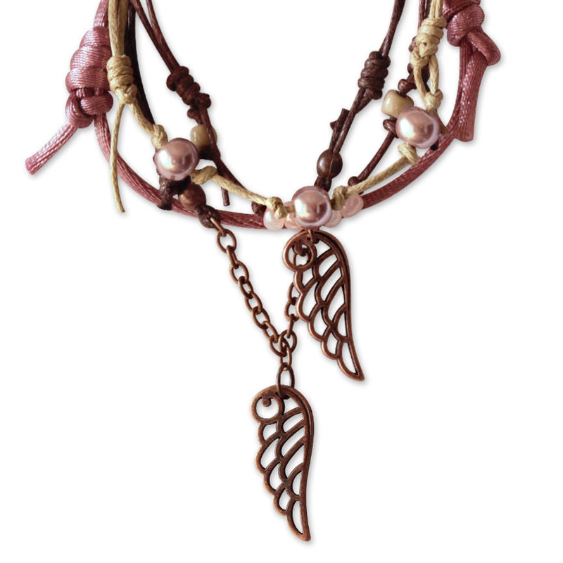 Close-up of bronze angel wing charm bracelet with pearl and knot details – boho celestial jewelry for layering and gifting.