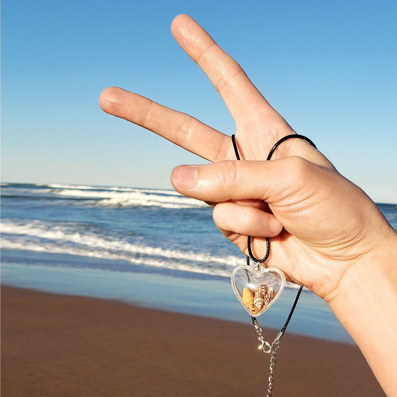 Clear heart locket necklace filled with sand and 3 beach shells – cowrie and spiral shells on black cord at the beach
