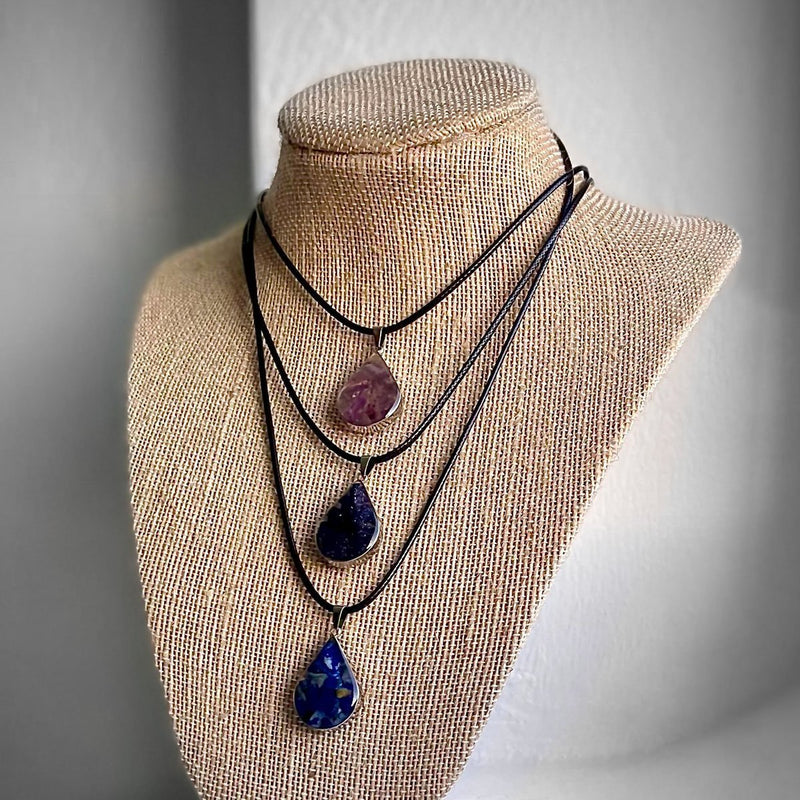 Teardrop crystal necklaces displayed on a bust – gemstone jewelry in amethyst, lapis lazuli, and druzy styles.
