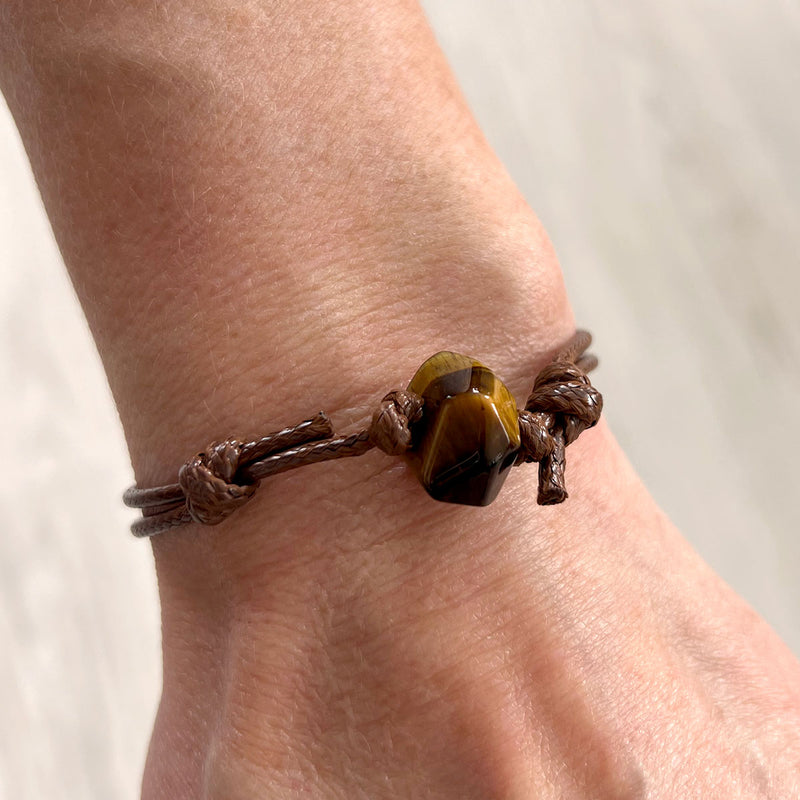 Close-up of tiger eye stone bracelet with brown cord – gemstone jewelry symbolizing courage and strength.